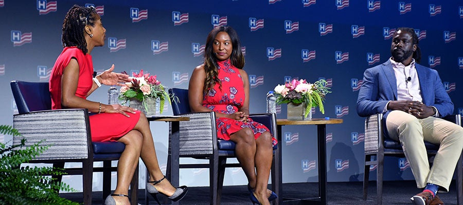 Two-women-and-a-man-are-seated-onstage-in-a-semi-circle