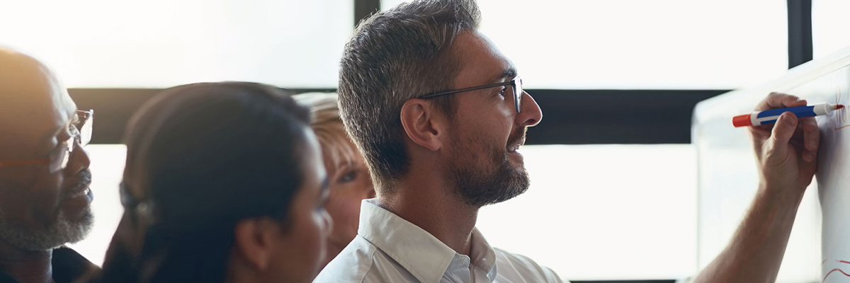 man writing on whiteboard with staff watching